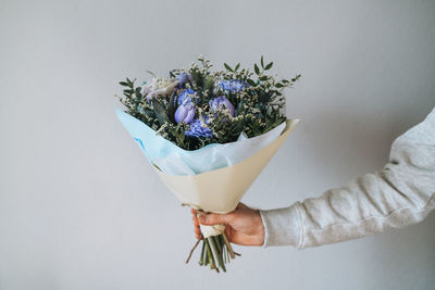 Young man in grey hoodie with bouqet of flowers in hands on the grey background