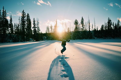 Man walking on snow covered land against sky during sunset