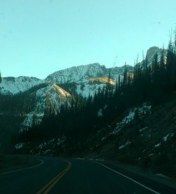 Road by mountains against clear sky during winter