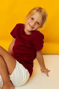 Portrait of young woman sitting against yellow background