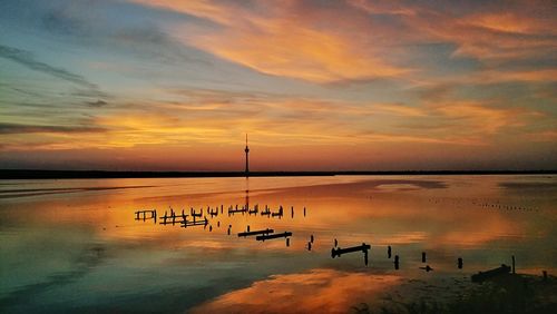 Wooden posts in sea against sky during sunset