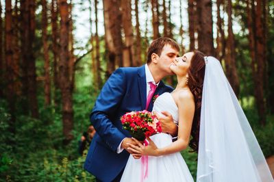 Bridegroom kissing bride against trees in forest