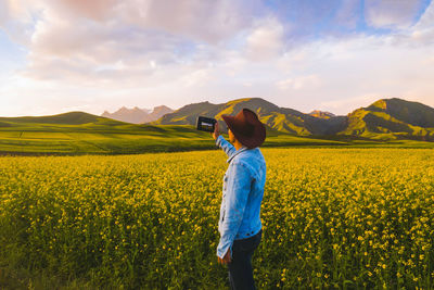 Man photographing while standing amidst flowering plants on field