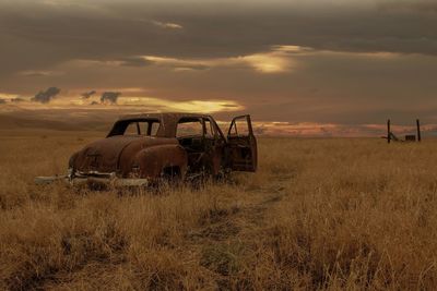 Abandoned vintage car on field against sky during sunset