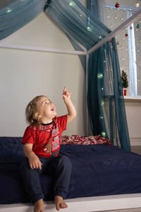 Portrait of boy sitting on bed at home