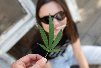 Cropped hand holding leaves by woman with cigarette