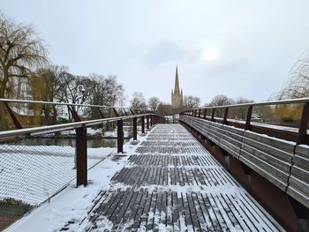 Footbridge amidst buildings against sky during winter