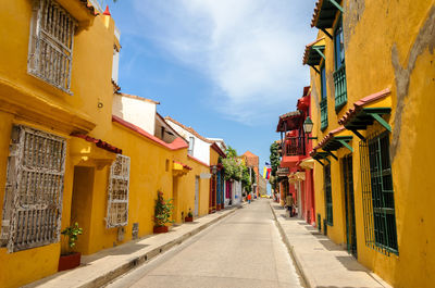 Street amidst yellow houses against sky on sunny day