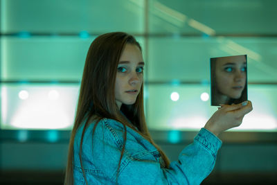 Portrait of woman holding mirror against wall