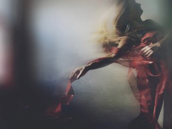 Blurred motion of woman wrapped in ribbon dancing against wall