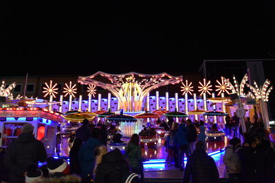 People at illuminated amusement park against sky at night