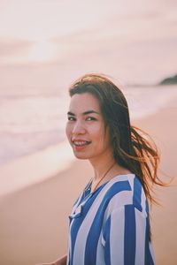 Side view portrait of smiling young woman standing at beach during sunset