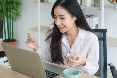 Young woman using phone while sitting on table