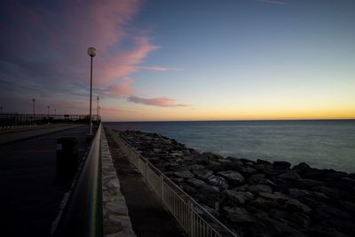 Street by sea against sky during sunset