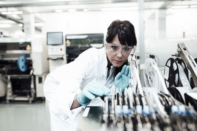 Mature female technician examining machinery in bright industry