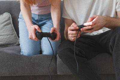 Midsection of man and woman playing video game while sitting on sofa