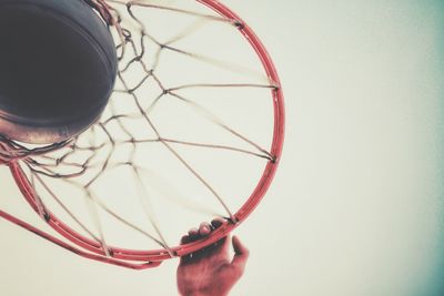 Cropped hand of man holding basketball hoop against clear sky