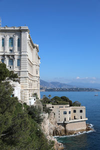 Buildings by sea against blue sky