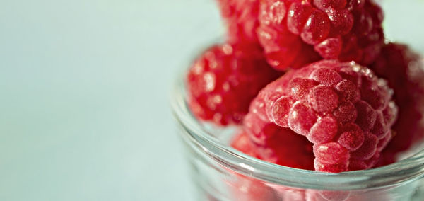 Frozen raspberries close-up in glass cup on blue background  copy space, healthy raw food vegan