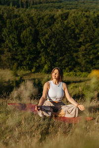 Young woman meditating on the mat outdoors at sunset with beautiful landscape on the background	
