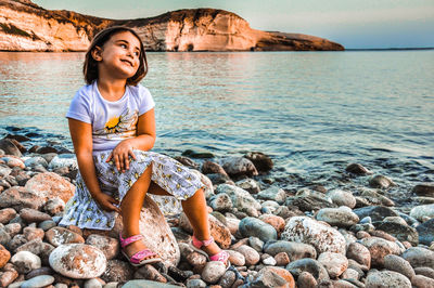 Full length of child sitting on rock at beach