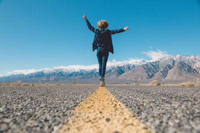 Rear view of woman on snowcapped mountain against blue sky