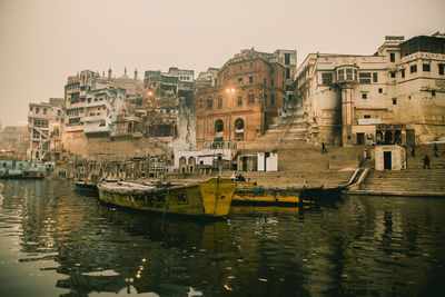 Boats in river by buildings in city against clear sky