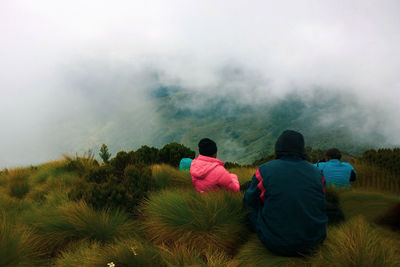 Rear view of people sitting on mount top  against foggy mountain 