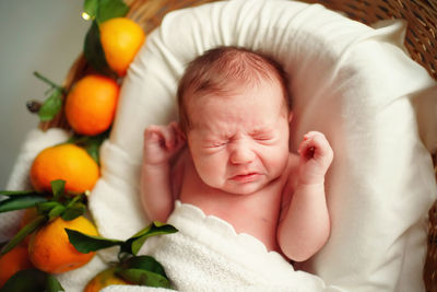 Caucasian newborn baby sneezes, lies in a basket with tangerines under a white blanket, allergic.