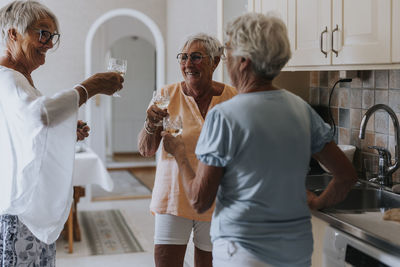Smiling senior woman having toast while standing and talking in kitchen