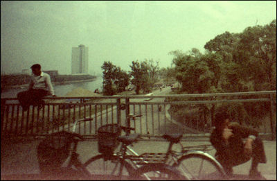 Man sitting on bicycle in city against sky