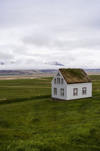 Typical nordic building with grass roof located on field against cloudy sky in countryside of iceland in hilly area