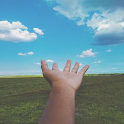 Midsection of person hand on field against sky