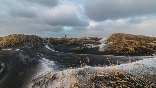 Scenic view of a photographer on the horizon in maze of grass covered black sand dunes