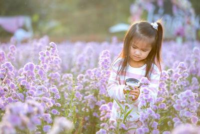 Close-up of girl holding magnifying glass by purple flowering plants