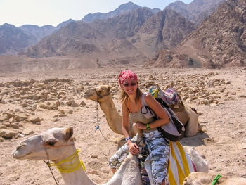 Portrait of woman riding camel at desert against mountains