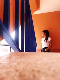 Thoughtful young woman looking away while standing against wall