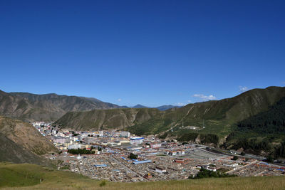Scenic view of townscape by mountains against clear blue sky