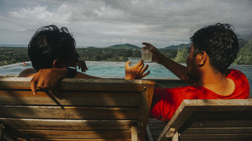 Rear view of men sitting on boat against sky