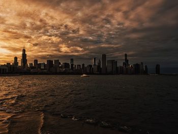 Sea and buildings against sky during sunset