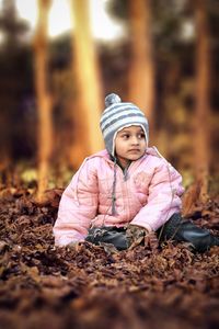Cute girl in warm clothing sitting on field