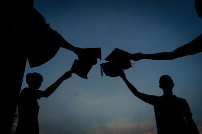Silhouette people holding hat against sky