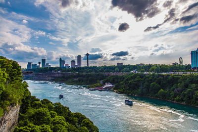 View of city at waterfront against cloudy sky