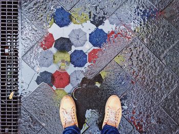 Low section of man standing by puddle with umbrellas reflection on footpath