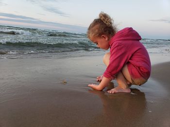 Girl playing with sand at beach during sunset