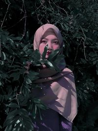 Portrait of a young woman standing against plants