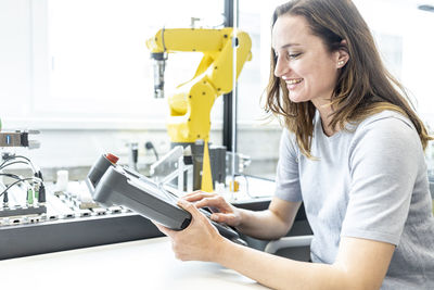 Female skilled worker in robotic factory controlling robot arm with digital control