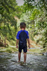 Rear view of boy standing in stream