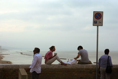 Rear view of people sitting by sea against sky