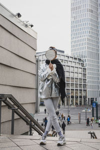 Young woman holding mirror while standing on steps in city